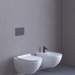 Vaso e bidet sospesi bianchi con placca di comando su parete grigia