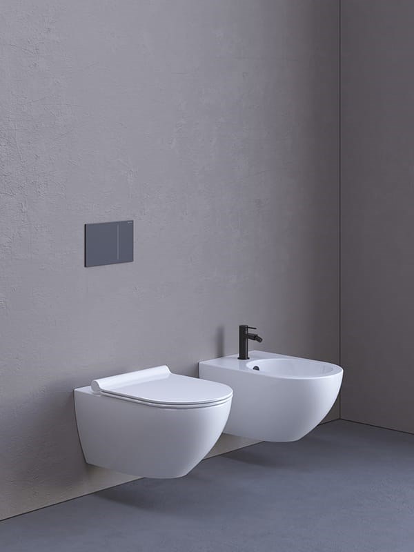 Vaso e bidet sospesi bianchi con placca di comando su parete grigia