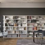 Libreria a tutta parete con ripiani bianchi, libri e poltrona