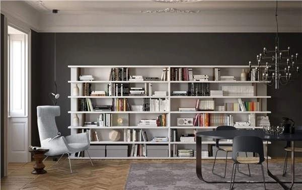 Libreria a tutta parete con ripiani bianchi, libri e poltrona