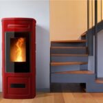 Stufa a pellet in maiolica rossa accesa accanto a una scala