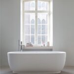 Vasca da bagno freestanding ovale bianca davanti a una finestra ad arco
