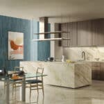 Cucina moderna con isola in marmo, pensili in legno e rivestimento Ceramica Del Conca Premiere, tavolo in vetro e legno.