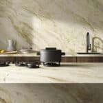 Cucina moderna con piano di lavoro e rivestimento in Ceramica Del Conca Premiere, piano cottura nero, lavello e rubinetto eleganti.