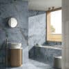 Bagno moderno con pavimenti e rivestimenti blu lucidi, lavabo su mobile rotondo in legno e vasca vicino a una finestra luminosa.