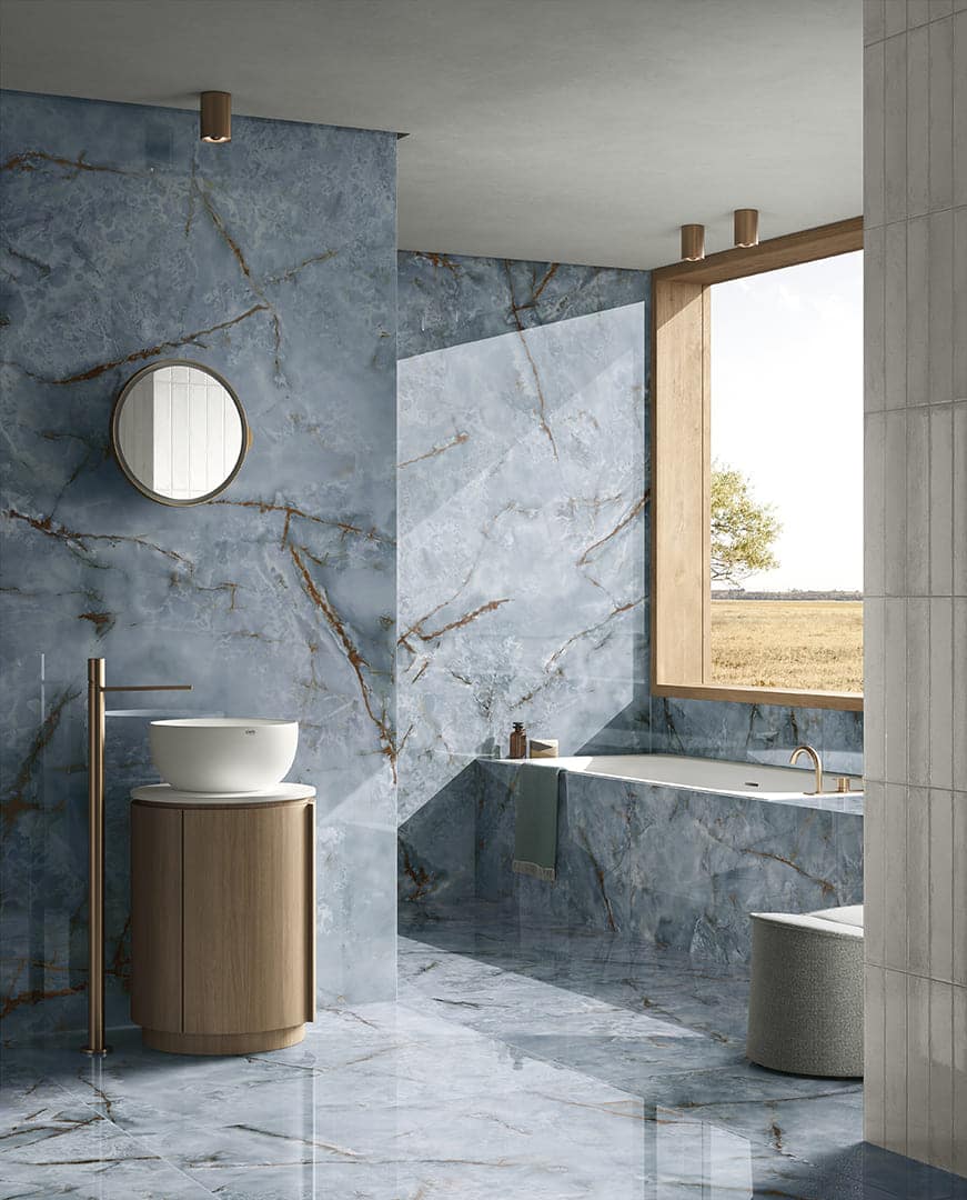 Bagno moderno con pavimenti e rivestimenti blu lucidi, lavabo su mobile rotondo in legno e vasca vicino a una finestra luminosa.