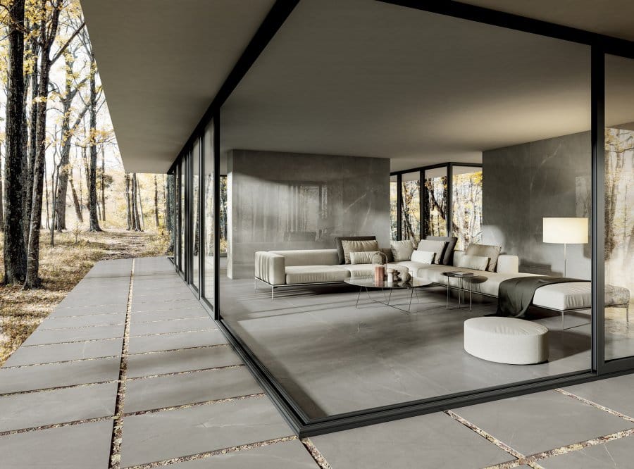 Soggiorno moderno con ampie vetrate, pavimento grigio della Ceramica Del Conca, divani bianchi e luce naturale.
