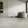 Pavimento e pareti in marmo della Ceramica Del Conca Boutique, pouf rotondo grigio e luce naturale che entra da un'ampia finestra.