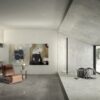 Zona giorno moderna con pavimento in marmo grigio della Ceramica Del Conca, parete inclinata e ampia finestra.