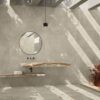 Bagno moderno con pareti e pavimento effetto cemento, lavabo sospeso in pietra, specchio rotondo e rubinetteria nera.