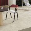 Tavolo rotondo in legno e sedia moderna su piastrelle beige della linea Timeline di Ceramica Del Conca, sedie bianche e piante verdi.