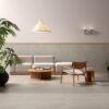 Salotto in stile minimalista con pavimento e pareti grigio chiaro, divano moderno, sedie in legno e tavolino rotondo.