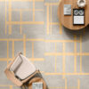 Poltrona beige e tavolini rotondi su piastrelle Ceramica Del Conca Sensoria con motivi geometrici gialli e grigi.