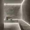 Hammam moderno con piastrelle Marble Edition di Del Conca, lavabo cilindrico in pietra e panca con asciugamani.