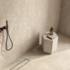 Doccia in stile minimalista in pietra beige con piastrelle Del Conca, soffione a parete e scarico lineare.