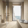 Bagno minimal in beige con vasca integrata, doccia walk-in e ampia finestra con vista sul mare. Piastrelle Stone Edition Del Conca.