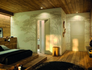 Camera da letto con pareti, pavimento e soffitto in legno, letto scuro, tappeto rotondo e due porte interne di design.
