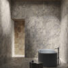 Bagno in stile minimalista con pareti in pietra, vasca ovale freestanding, rubinetto nero e rivestimenti Ceramica Del Conca Marble Edition.